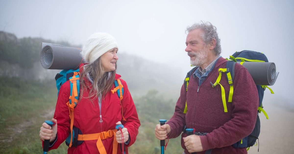 Couple de randonneurs âgés avec bâtons de marche dans la brume en montagne